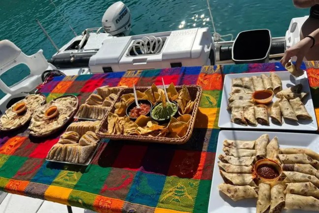 Mexican food spread on colorful tablecloth aboard a boat near water.