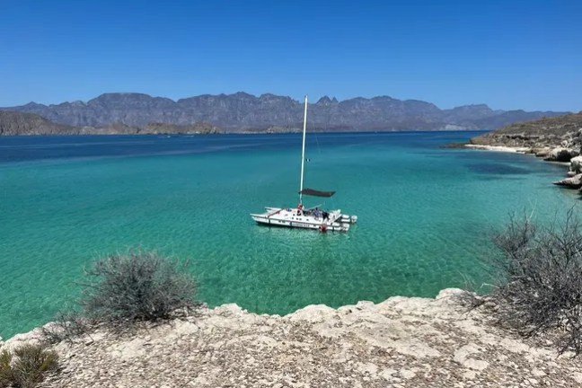 Sailboat on clear turquoise water with distant mountains under a blue sky.