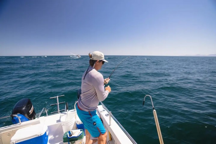Person fishing from a boat in the ocean under a clear blue sky.