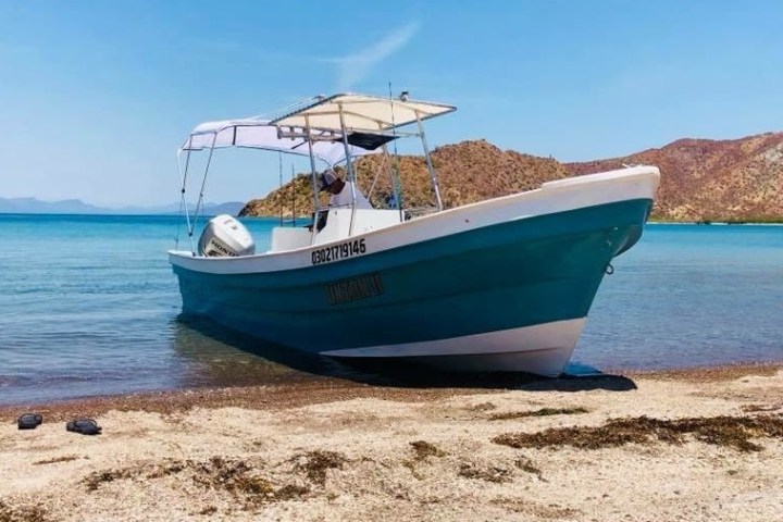 A small boat on a sandy beach with mountains in the background under a clear blue sky.