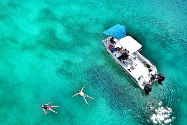 Boat and two people floating in clear turquoise water.